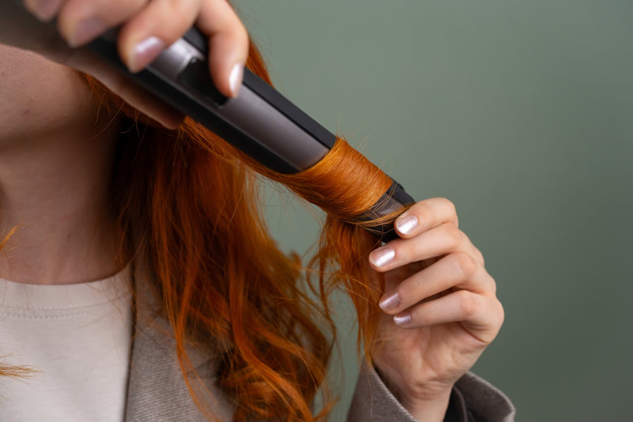 about-img Close-up of a woman curling her vibrant red hair with a curling iron.