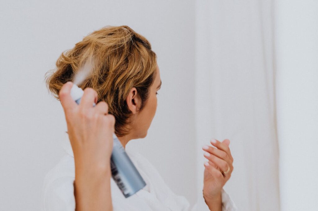 A woman uses hair spray for styling in a bright indoor setting.