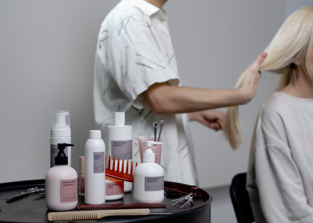 A hairdresser styling a blonde woman's hair in a salon, showcasing hair care products on a table.